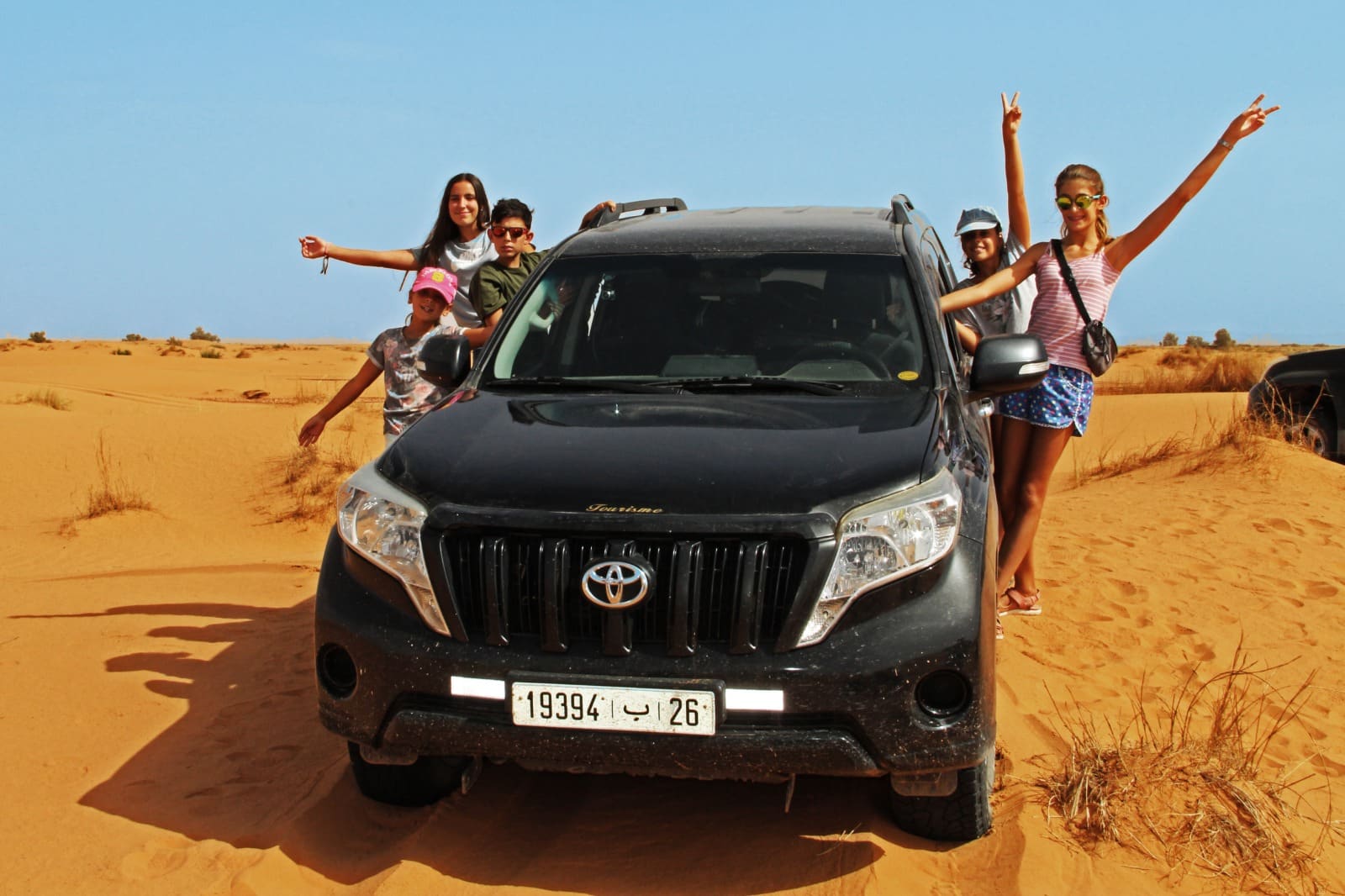 Niños sonrientes y emocionados en un vehículo 4x4 privado recorriendo las dunas de Erg Chebbi durante un viaje a Marruecos en familia.